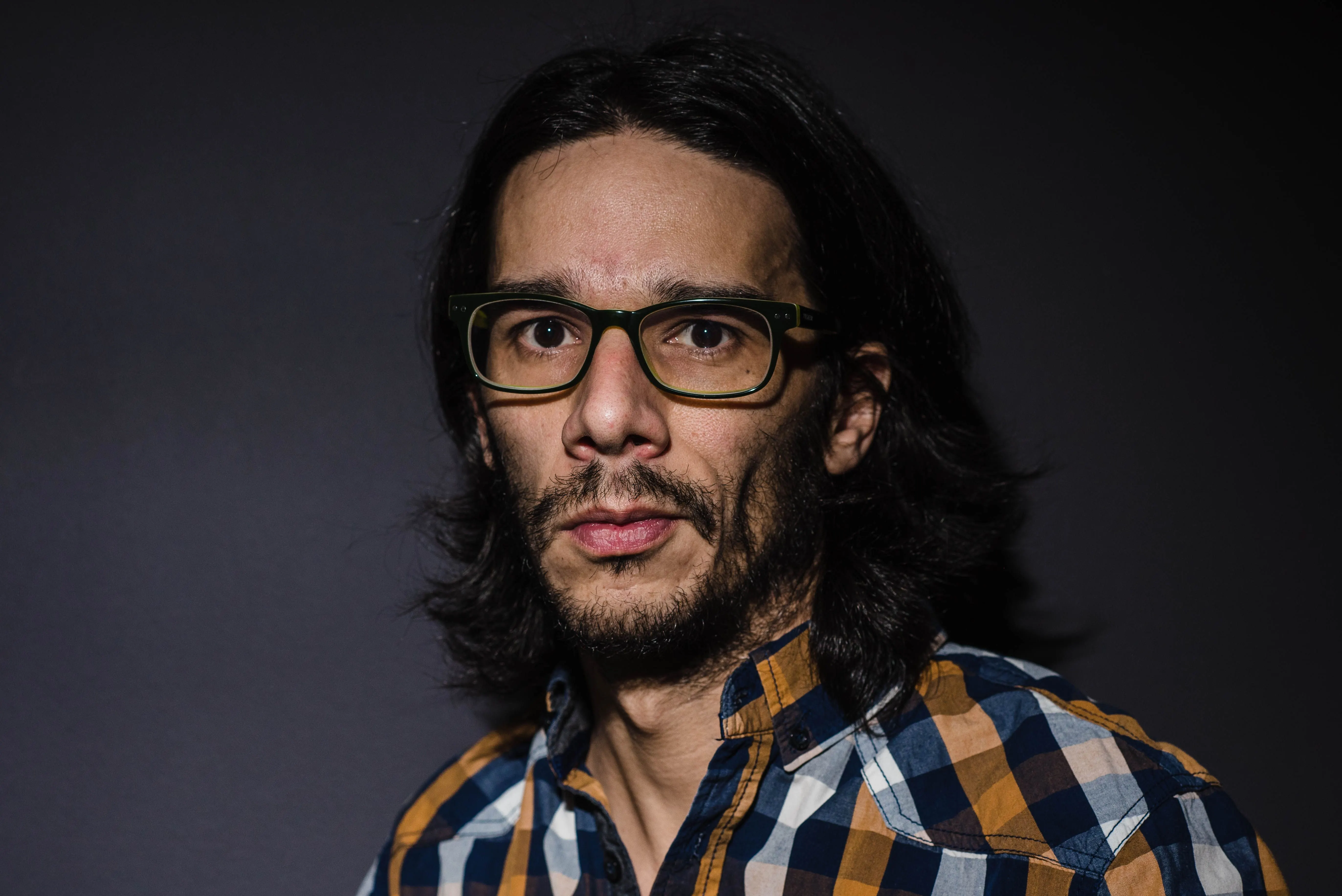 Retrato de Juan Carlos Blanco, fotógrafo de bodas en Ávila, con gafas y camisa de cuadros sobre fondo oscuro