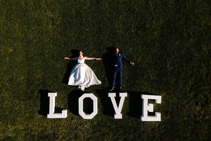 Natalia y Rubén tumbados en el césped junto a letras gigantes de LOVE, vista cenital